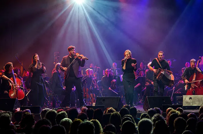 Grand orchestre sur scène entouré de musiciens et d'un public dense